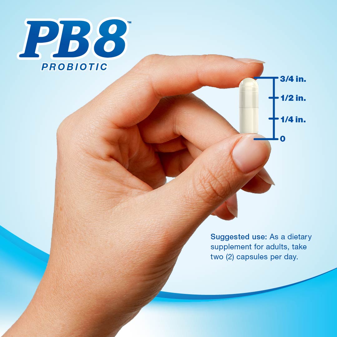 A hand holding a PB8 Probiotic capsule, measuring 3/4 inch long.