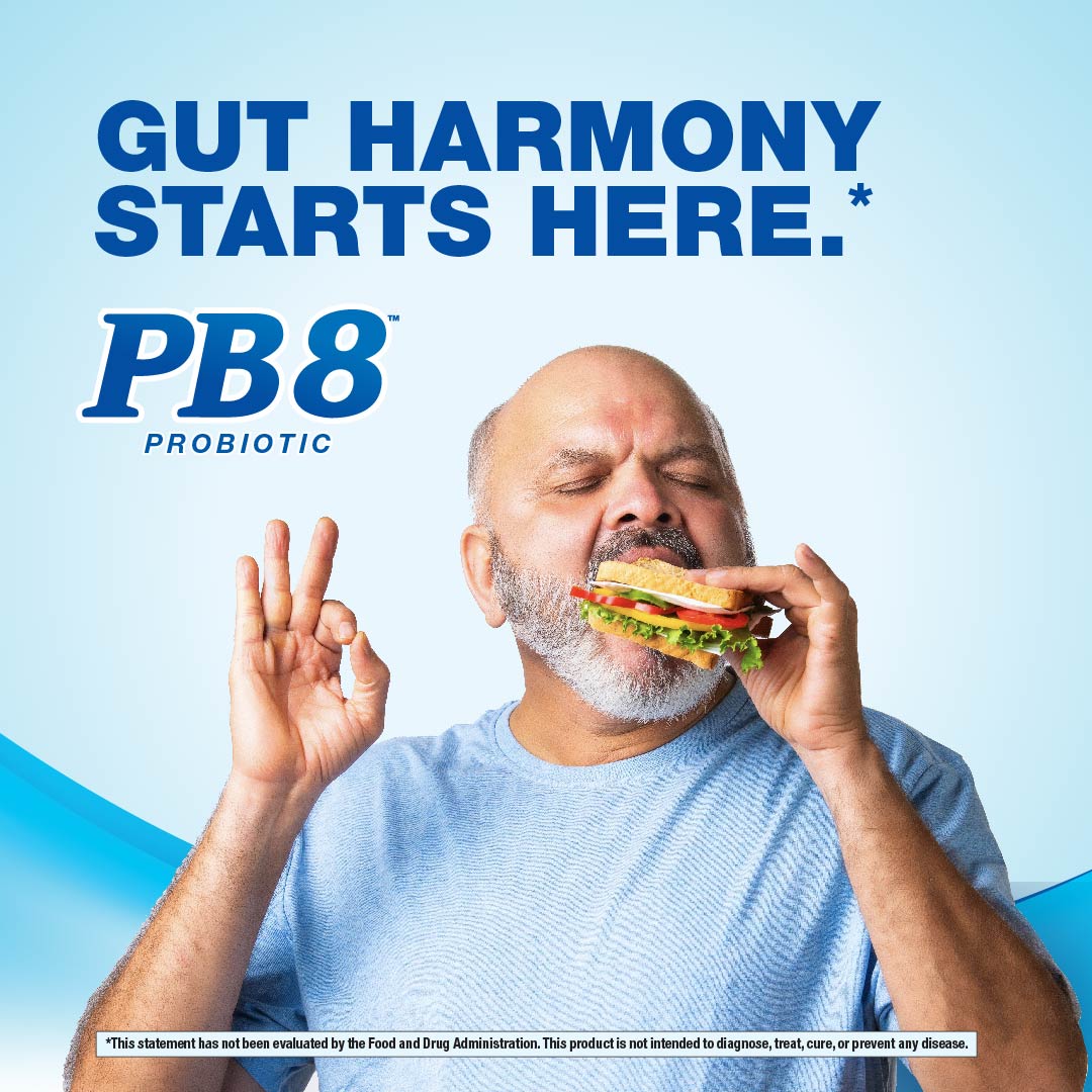 Older man happily eats a sandwich and makes an OK gesture, with visible PB8 Probiotic text in the background.